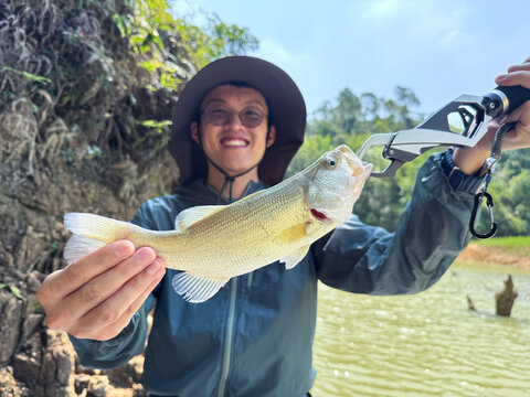 Man Holding Freshly Caught Fish by Lake