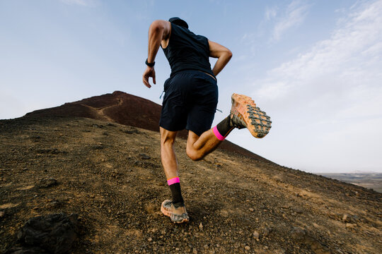 Rear perspective of an athlete ascending a rocky volcanic slope