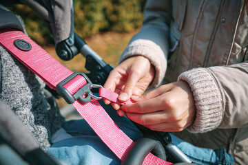 Close-up of caring hands securing a vibrant pink safety strap on a stroller, ensuring child protection and family well-being during outdoor activities. Emphasizes responsible parenting, security, a