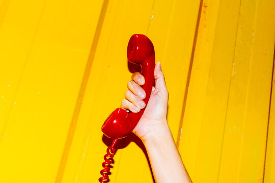 man holding red telephone receiver on yellow wall