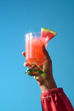 A hand holding a refreshing watermelon cocktail under a vibrant blue