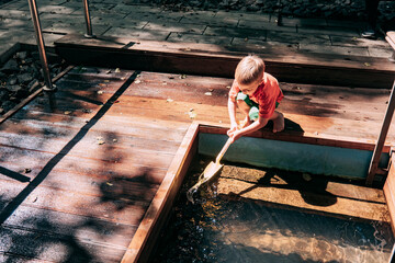 Child playing with water near a wooden platform on a sunny day