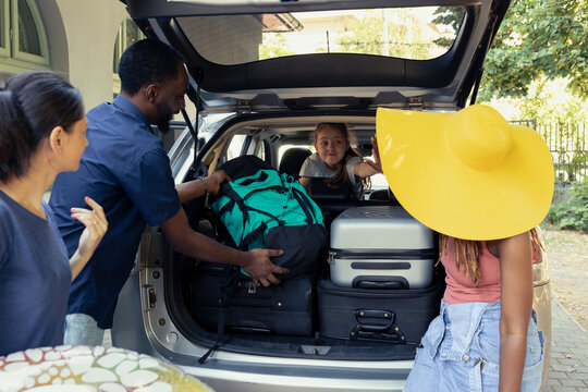 In the warm sun, black couple with a mom and little excited girl enjoy packing their automobile for a relaxing getaway. Their holiday trip includes inflatable toys and relaxing energy.