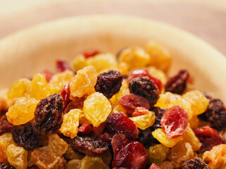 A bowl of dried fruit with yellow and red raisins, cranberries. The bowl is on a wooden table. Natural high sugar and glucose content. Popular snack.