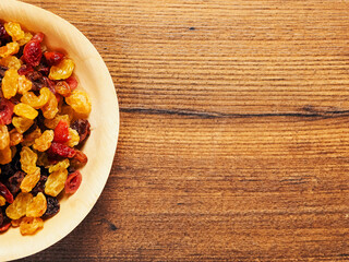 A bowl of dried fruit with yellow and red raisins, cranberries. The bowl is on a wooden table. Natural high sugar and glucose content. Popular snack.