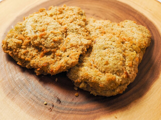 Breaded chicken breast fillet on a wooden board. Classic poultry product. Uncooked meat covered with golden breadcrumbs.