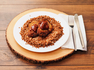 Simple tasty buckwheat and breaded chicken fillet with barbeque sauce meal on a white round plate and round wooden serving board and wooden table. Popular Russian dish..