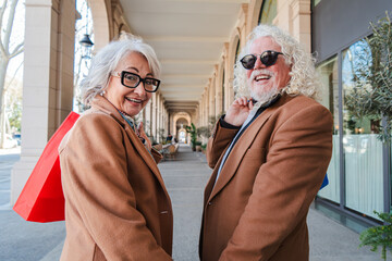 A cheerful senior couple joyfully engaging in a delightful shopping adventure, smiling brightly as they stroll together, showcasing their enthusiasm for life, love, and the thrill of exploring new