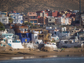 CLOSE UP: Scenic coastal town with colorful houses and surfers on the beach. Vibrant blend of...