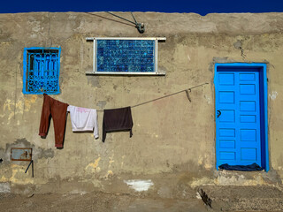 CLOSE UP: Rustic wall of an older house with blue window and door, hanging clothesline and solar panel. Touch of modernization and sustainability while traveling through simple Moroccan villages.