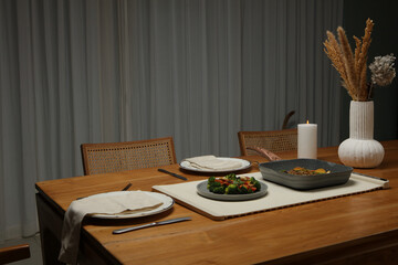 A modern dining table is set for two, with a meal and a lit candle. The image highlights a cozy and inviting atmosphere for a home-cooked dinner, perfect for a relaxed evening