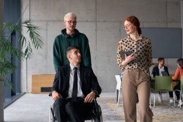 A diverse team of business colleagues, including a director in a wheelchair, engages in a collaborative discussion as they move together through a modern office space