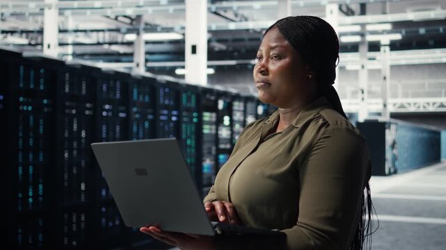 Data center workplace programmer using laptop to coordinate deployment of new server architecture. Server room worker using notebook to do rollout of cybersecurity framework, protecting data, camera A