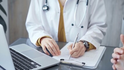 Doctor completing paperwork with patient. Close-up of a doctor's hands with forms, imparting information to a laptop. Medicine and health care concept