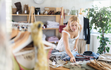 Young woman has come to a European clothing store, she is standing near counter and choosing pants and trousers among the clothes. Woman on shopping in the mall