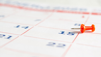 A red thumbtack on a calendar page. Business concept.