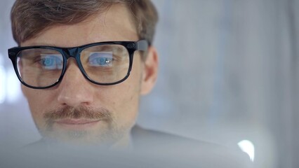 Businessman with glasses looking intently obscured partially by a translucent surface of laptop....