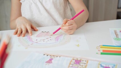 Close-up of a child's hands coloring a drawing with bright pencils. Young girl engaging in colorful...