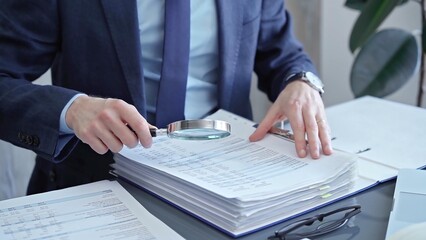 Adult businessman or auditor examining documents with magnifying glass. Professional in a suit...
