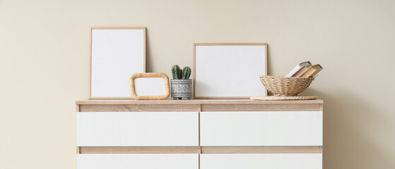 Chest of drawers with frames and decor near beige wall in room