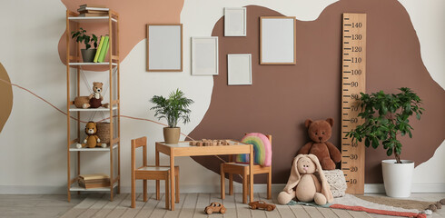 Interior of children's room with blank frames, stadiometer, table and shelving unit