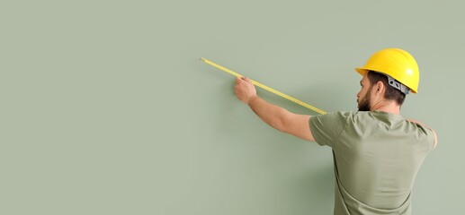Male worker measuring green wall, back view. Banner for design