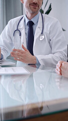 Doctor consulting patient. Male physician is gesturing above a clipboard while talking with a woman in a clinic, close up