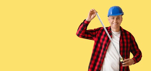Male construction worker holding tape measure on yellow background with space for text