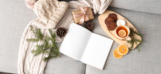 Blank book with winter accessories, Christmas gift and tea on sofa, top view