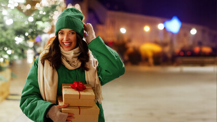 Happy woman holding gift boxes standing near decorated Xmas tree, walking and enjoying Christmas...