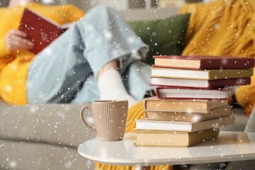 Stack of books with cup on table near woman reading Christmas story at home