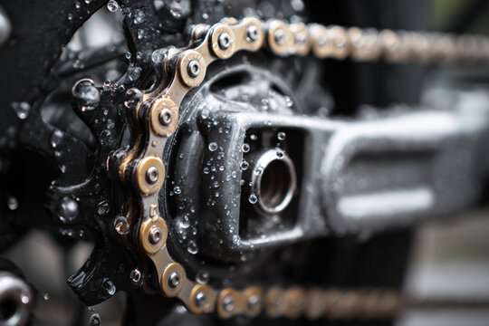 Bicycle chain and gear covered in water droplets after cleaning in a well-lit workshop