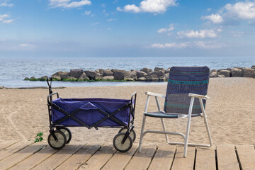 A four wheel beach wagon by a folding beach chair  on a board walk by the water. © SockaGPhoto