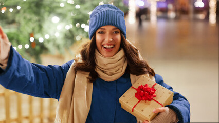 Happy young European woman with gift boxes in hands posing outside on Christmas Eve, taking selfie with decorated festive background. Concept of shopping and holidays © Home-stock