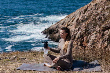 Woman practicing meditation and stretching on yoga mat by the ocean, surrounded by nature, enjoying tranquility and mindfulness in a serene outdoor environment with copy space