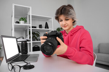 Naklejka premium Beautiful young happy female photographer with professional camera and laptop working at table in studio