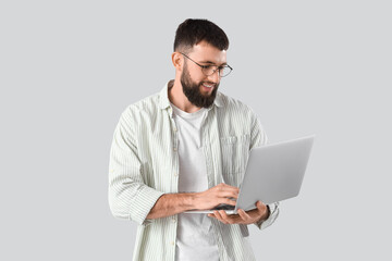 Young bearded man using laptop on light background
