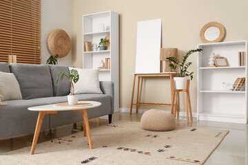 Grey sofa with houseplants and empty poster near beige wall in living room