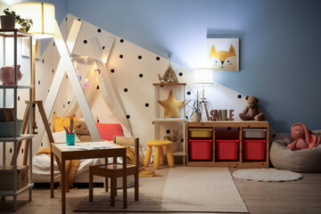 Interior of stylish children's bedroom with cozy bed, toys, glowing lights and lamps at night