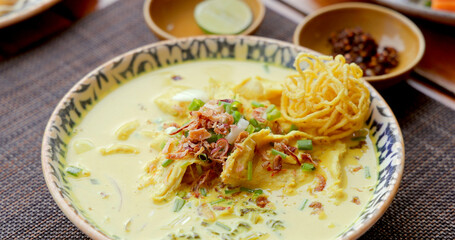 Thai Khao Soi curry noodles in decorative bowl. Authentic Chiang Mai cuisine garnished with shallots and lime on rustic mat. Asian food concept, spicy soup.