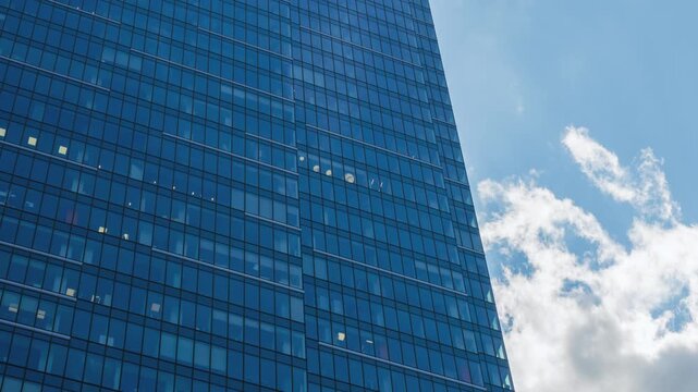 Low angle close-up time-lapse of downtown high-rise glass skyscraper on sunny day, financial district looking up tall modern architecture office building city center street, blue sky white clouds