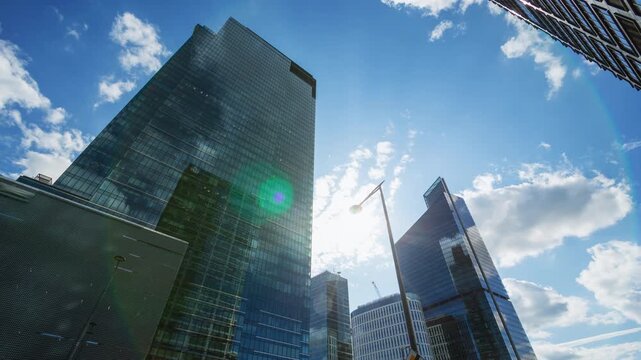 Low angle time-lapse of downtown high-rise glass skyscrapers on sunny day, financial district looking up tall modern architecture office buildings city center street, sunlight blue sky white clouds