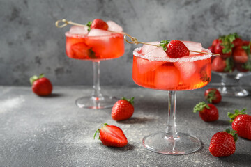 Glasses of drink with ice cubes and strawberries on grey grunge background