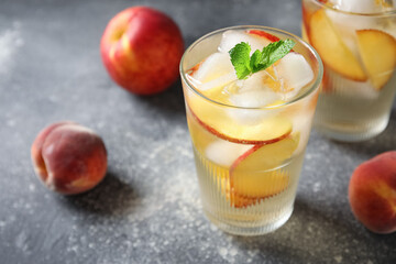 Glasses of drink with peach slices, ice cubes and mint leaves on grey grunge background