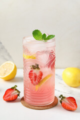 Glass of drink with ice cubes, strawberry and lemon slices on marble background