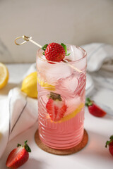 Glass of drink with ice cubes, strawberry and lemon slices on marble background