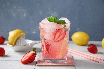 Glass of drink with ice cubes, mint leaves, strawberry and lemon slices on tile table against blue wall