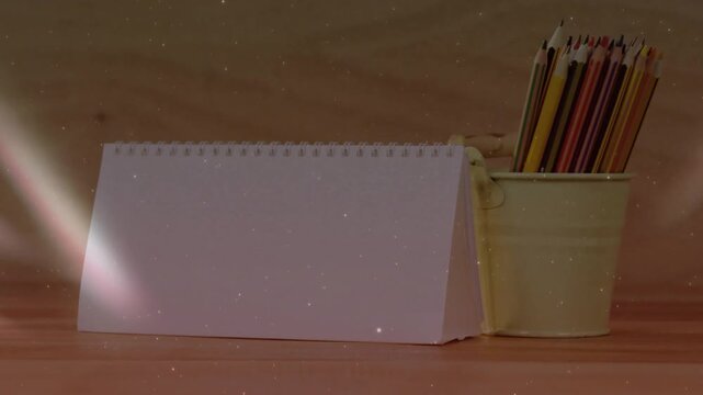 Colored light beams sweeping across desk highlighting white calendar beside yellow pencil holder