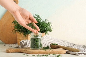 Female hand with jar and wooden spoon of fresh green dill on white background