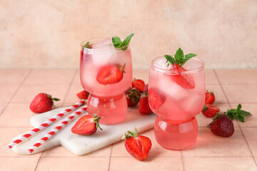 Glasses of tasty cold cocktail with strawberry on pink tile table near wall, closeup